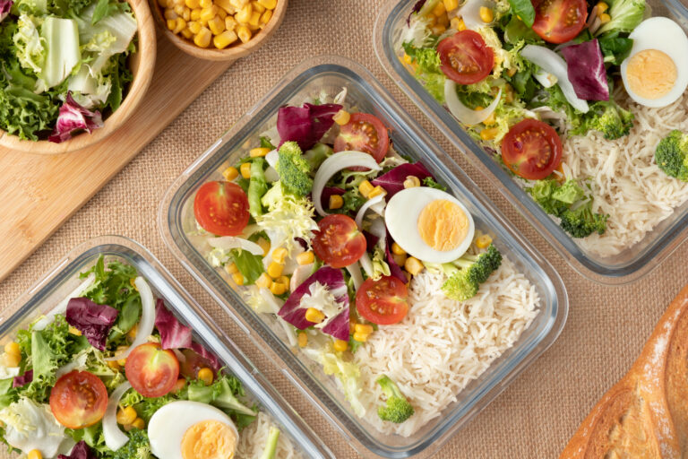 Marmitas com arroz, ovo, salada, tomate e milho, mostrando organização e variedade na alimentação