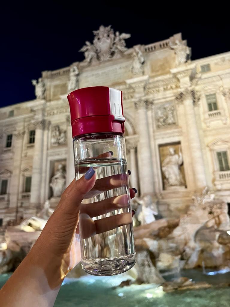 Pri segurando garrafa de água na Fontana di Trevi, representando a importância da hidratação durante a viagem